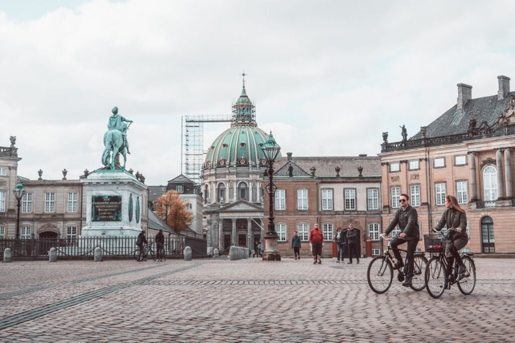 Aged masonry cathedral and sculpture near buildings on tiled pavement with walking people in Copenhagen